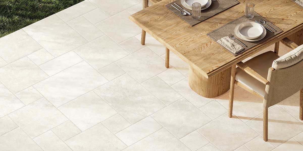 Outdoor dining area featuring Pietra di Trani Biancone porcelain tile in a modular stone pattern.