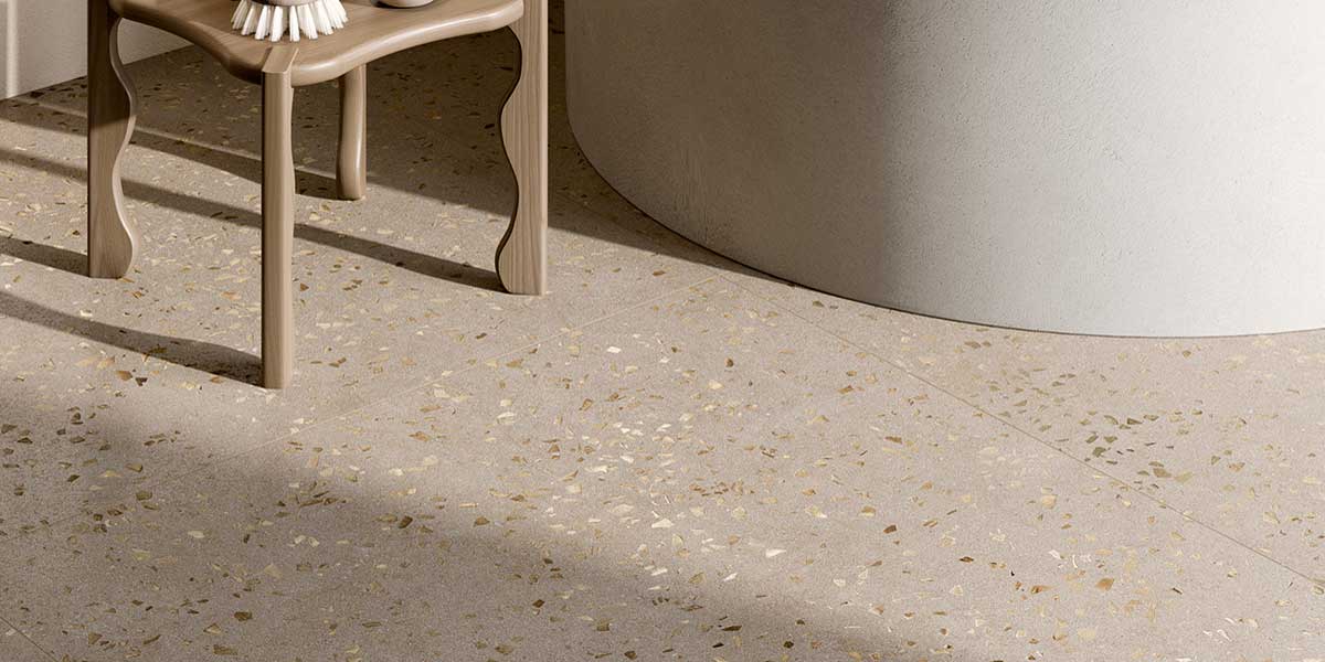 Close-up of Bits Greige terrazzo-look porcelain floor tile surrounding a freestanding bathtub.