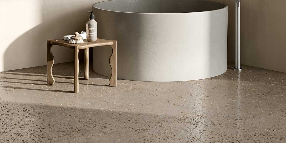 Bits Greige terrazzo-look porcelain floor tile in a minimalist bathroom with freestanding tub.